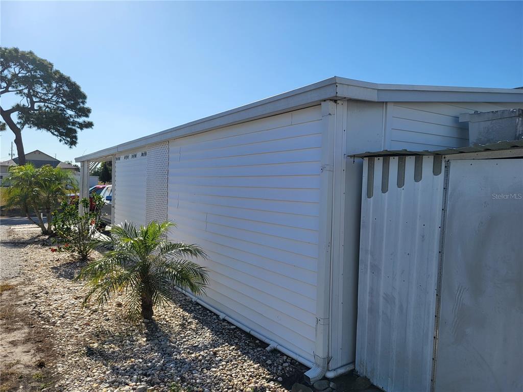 The exterior side of a white mobile home features horizontal siding and a metal shed — 12017 CARTWRIGHT DRIVE, HUDSON, FL