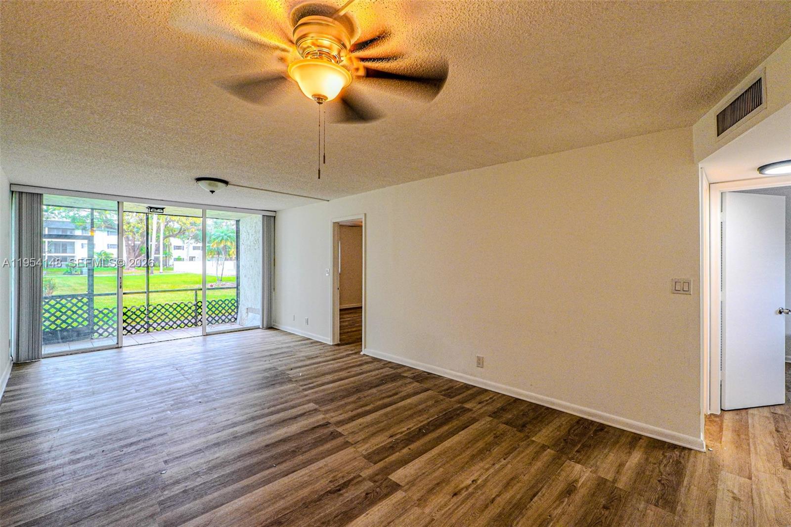 An empty living room features wood-look flooring, a ceiling fan, and a sliding glass door — 5100 SW 64th Ave # 106, Davie FL 33314, DAVIE, FL
