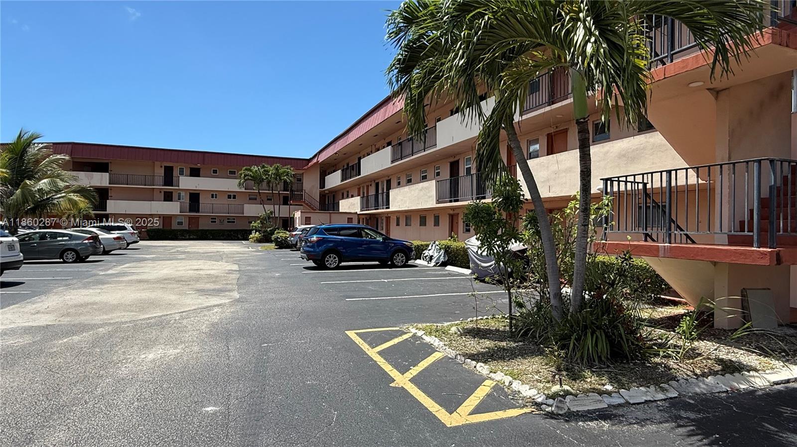 An exterior view of a multi-story apartment complex with a parking lot and palm trees — 19001 NE 14th Ave # 145, Miami FL 33179, MIAMI, FL