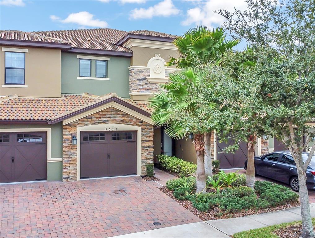 A two-story townhouse with a stone facade, brown garage doors, and a brick driveway — 9038 AZALEA SANDS LANE UNIT 1, DAVENPORT, FL