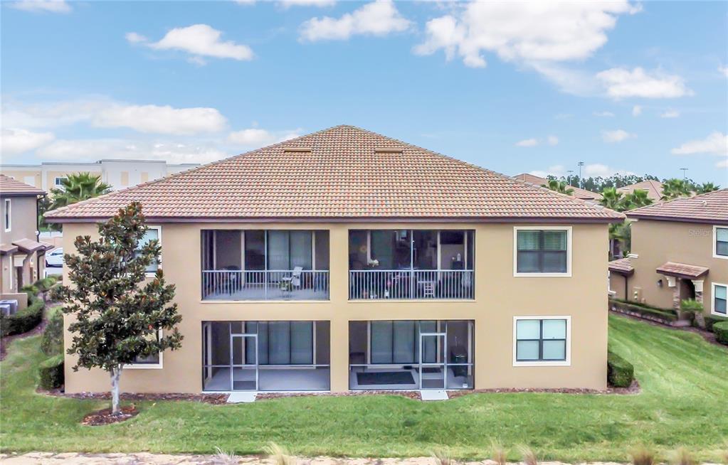 The rear exterior of a two-story tan building features screened-in balconies and patios — 9038 AZALEA SANDS LANE UNIT 1, DAVENPORT, FL