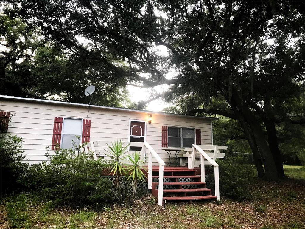 A single-story house with light siding, red shutters, and a wooden front deck — 118 MILLCREEK DRIVE, MELROSE, FL
