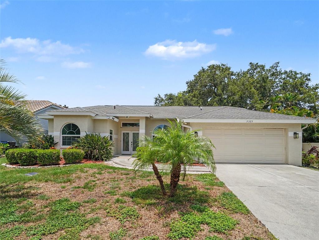 A single-story house with a beige stucco exterior, a two-car garage, and a palm tree — 5325 GARDENS DR, SARASOTA, FL