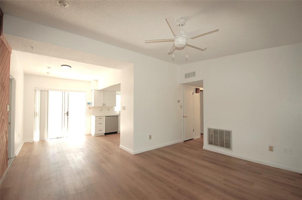 An interior view of a living room with light wood flooring and an adjacent kitchen — 1201 S BETTY LANE, CLEARWATER, FL
