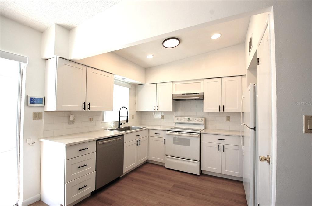A kitchen features white cabinets, stainless steel appliances, a subway tile backsplash, and wood flooring — 1201 S BETTY LANE, CLEARWATER, FL