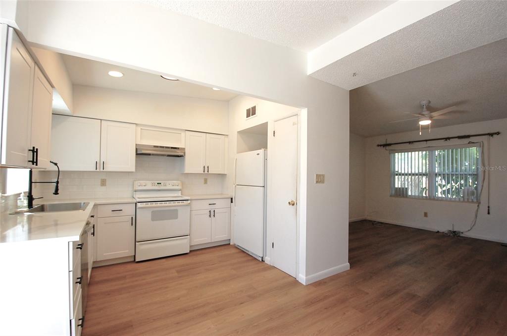 A kitchen with white cabinets and appliances opens into a living area with wood flooring — 1201 S BETTY LANE, CLEARWATER, FL