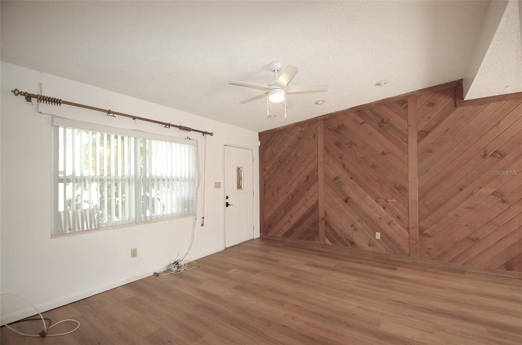 A living room features wood-paneled accent walls, light wood flooring, and a ceiling fan — 1201 S BETTY LANE, CLEARWATER, FL