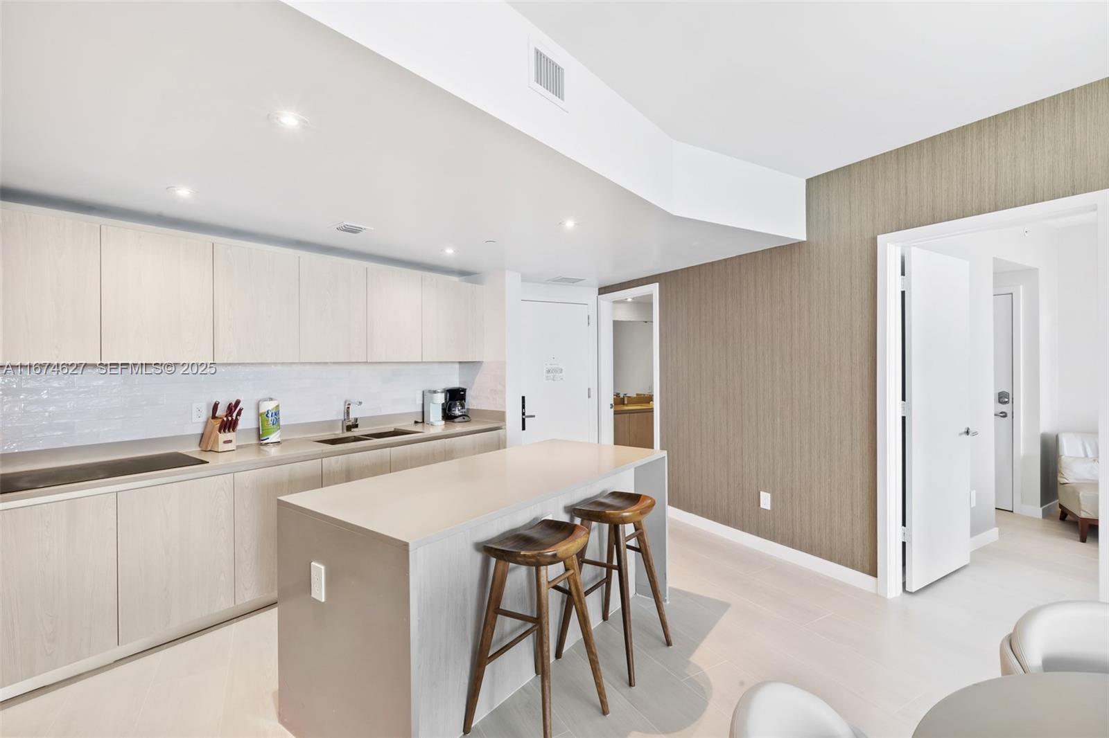 A modern kitchen features light wood cabinetry, a central island with bar stools, and tile flooring — 4111 S Ocean Dr # 3108, Hollywood FL 33019, HOLLYWOOD, FL