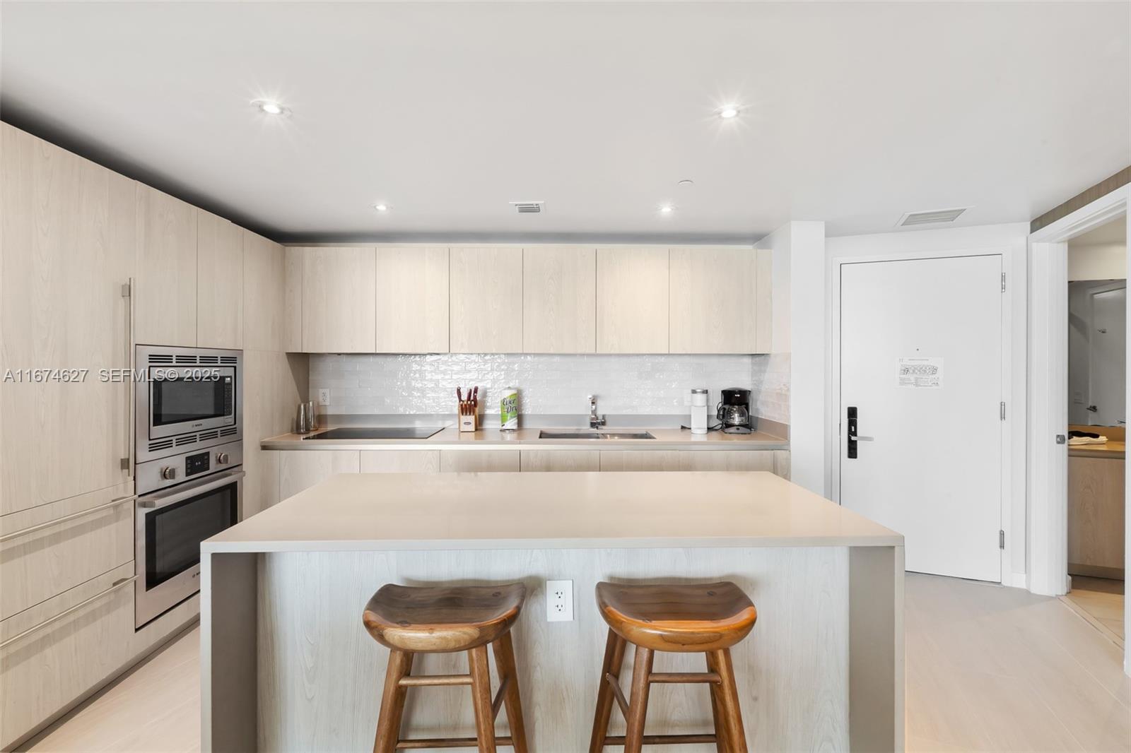 A modern kitchen features light wood cabinetry, a central island with two stools, and stainless appliances — 4111 S Ocean Dr # 3108, Hollywood FL 33019, HOLLYWOOD, FL