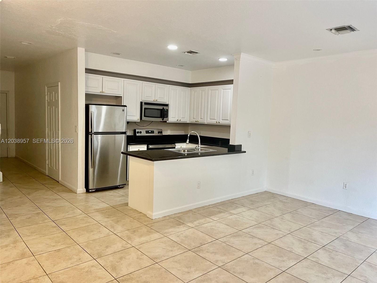 A kitchen features white cabinets, stainless steel appliances, a black countertop, and tiled flooring — 35 SE 3rd Ave # 11, Hallandale Beach FL 33009, HALLANDALE BEACH, FL