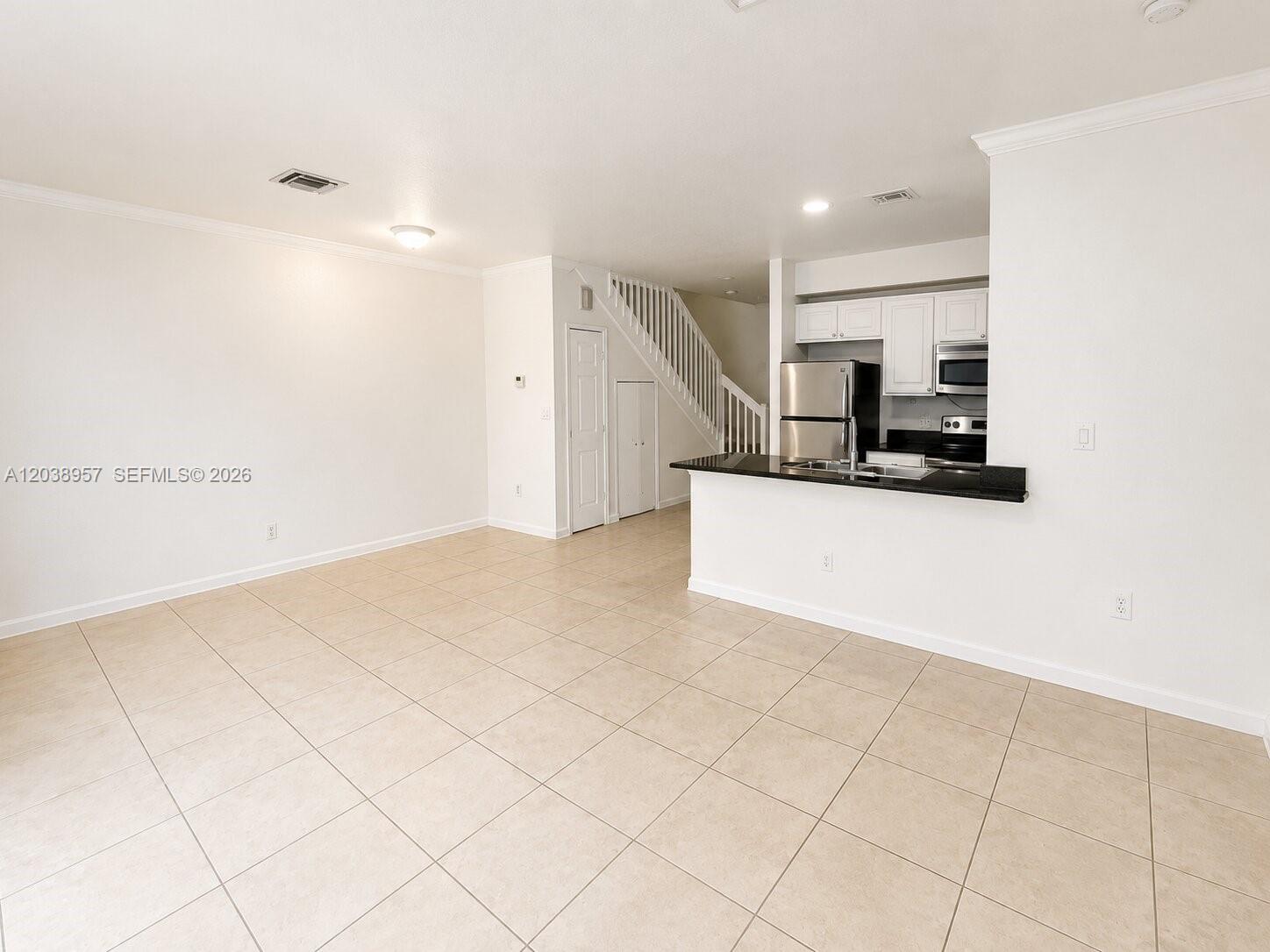 An open-concept living area features light tile flooring, a kitchen with dark counters, and stairs — 35 SE 3rd Ave # 11, Hallandale Beach FL 33009, HALLANDALE BEACH, FL