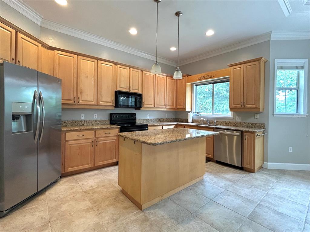 A kitchen features light wood cabinets, granite countertops, a center island, and stainless steel appliances — 14424 NW 22ND PLACE, NEWBERRY, FL