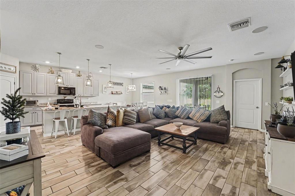 An open-concept living room and kitchen featuring tile flooring, a large sectional, and light cabinetry — 13968 NESBIT COURT, HUDSON, FL