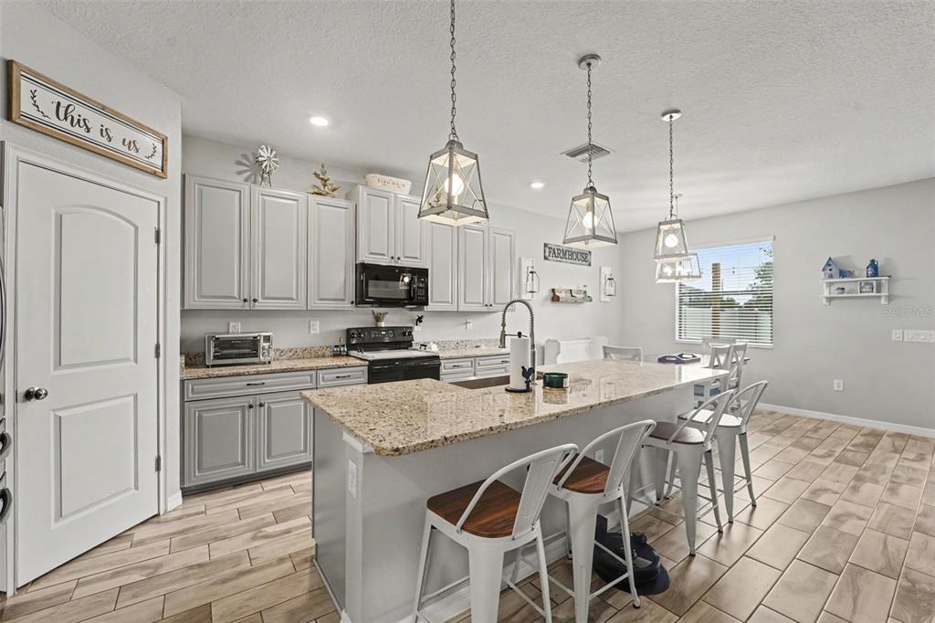 A kitchen features gray cabinets, granite countertops, a central island with bar seating, and tile flooring — 13968 NESBIT COURT, HUDSON, FL