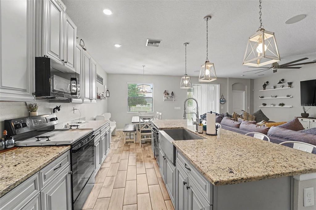 A kitchen with grey cabinets, granite countertops, a farmhouse sink, and a dining area — 13968 NESBIT COURT, HUDSON, FL