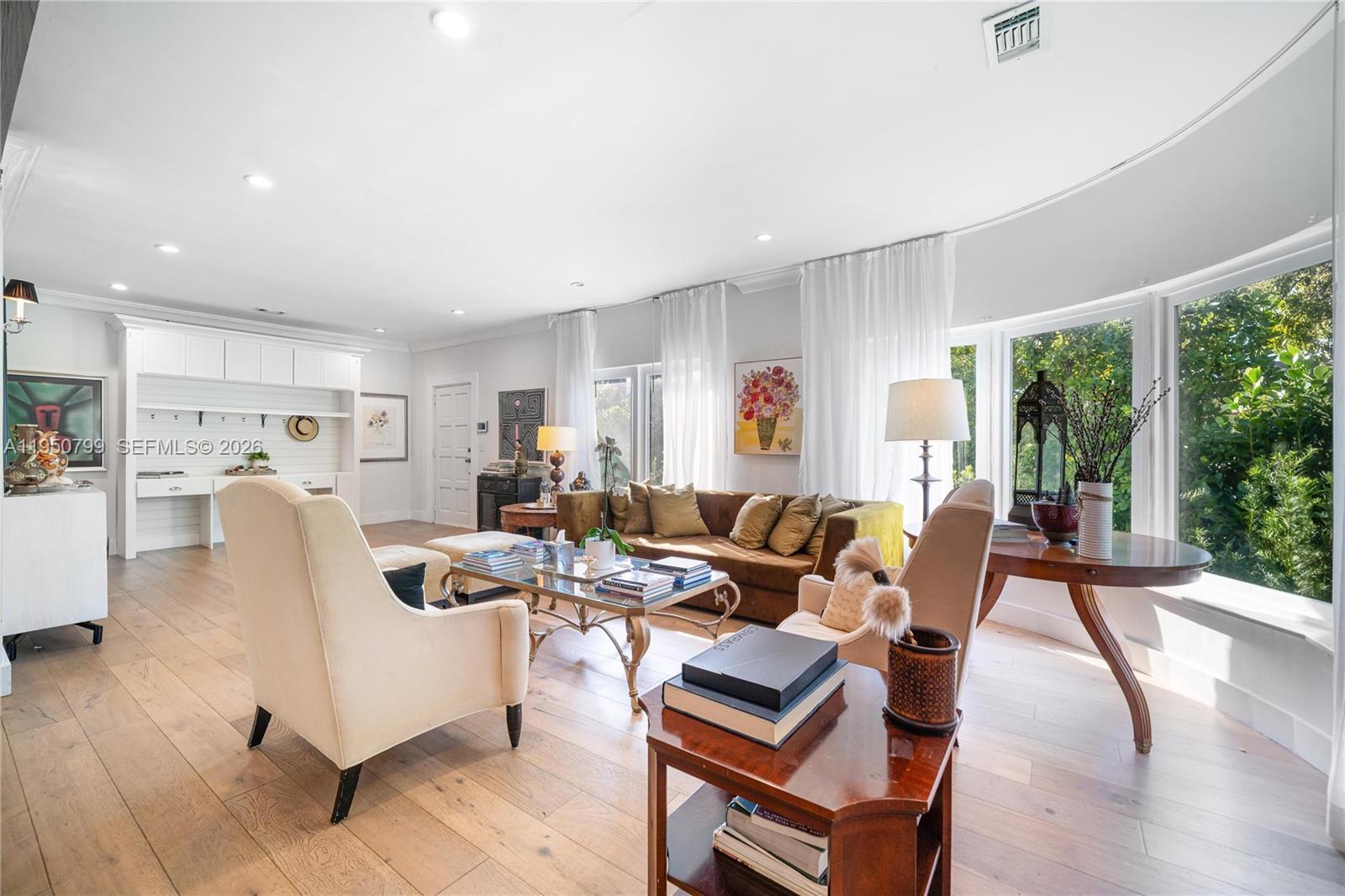 A bright living room features light wood floors, a curved window wall, and built-in shelving — 463 W 62nd St, Miami Beach FL 33140, MIAMI BEACH, FL