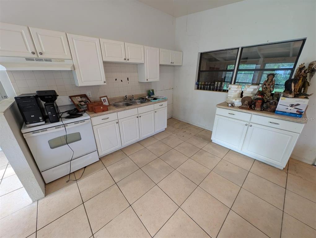 A kitchen features white cabinets, a white stove, a double sink, and tiled flooring — 765 GREENWAY PLACE, DAYTONA BEACH, FL