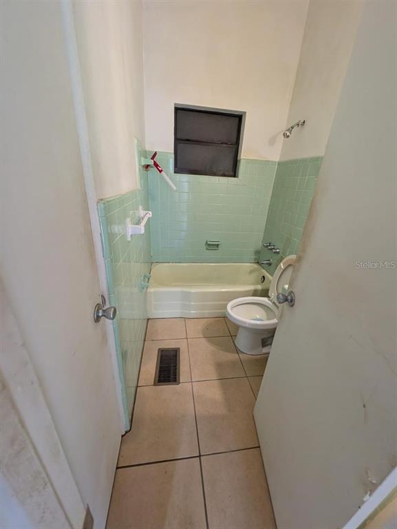 A small bathroom features light green wall tiles, a white bathtub, and a toilet — 765 GREENWAY PLACE, DAYTONA BEACH, FL