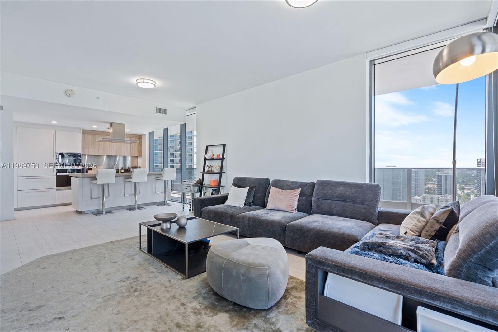 A modern living room with a gray sectional sofa, coffee table, and an open kitchen — 1000 Brickell Plz # 2812, Miami FL 33131, MIAMI, FL
