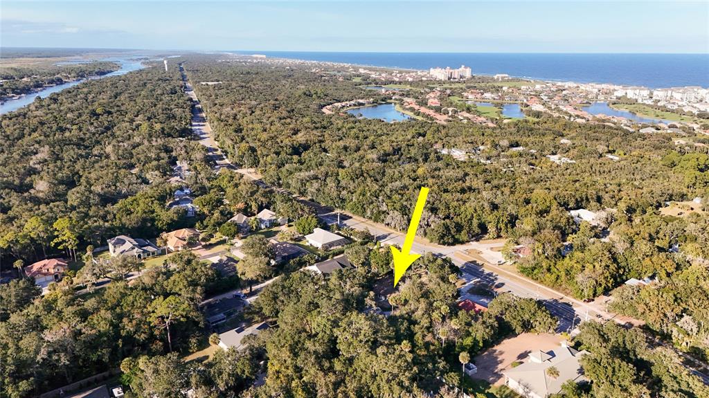 An aerial view shows a wooded residential area with a yellow arrow pointing toward a house — 5062 N OCEAN SHORE BOULEVARD, PALM COAST, FL