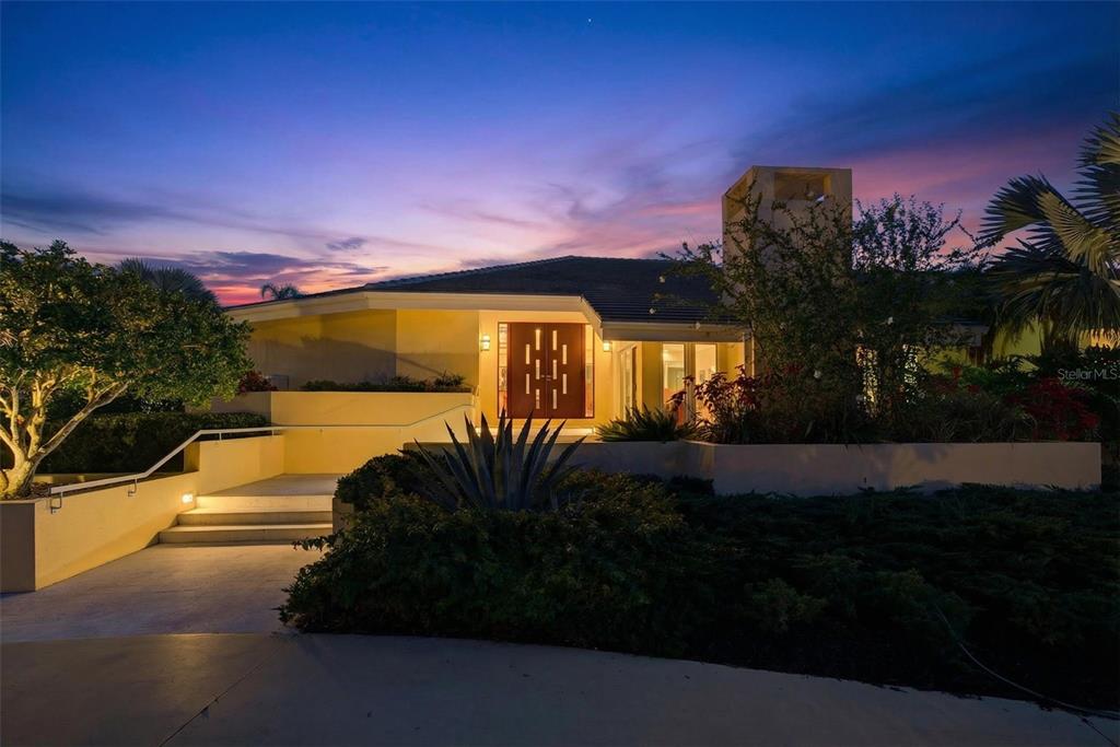 A modern house exterior with a prominent front door and steps at twilight — 1571 HARBOR CAY LANE, LONGBOAT KEY, FL