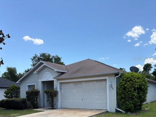A single-story house with a two-car garage, light-colored stucco walls, and a shingled roof — 1584 FUJI DRIVE, TITUSVILLE, FL