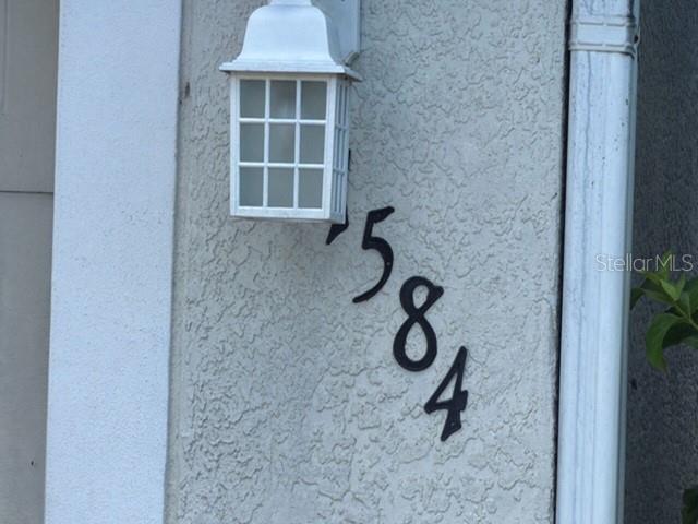 A white outdoor light fixture is mounted above the black house numbers 1584 — 1584 FUJI DRIVE, TITUSVILLE, FL