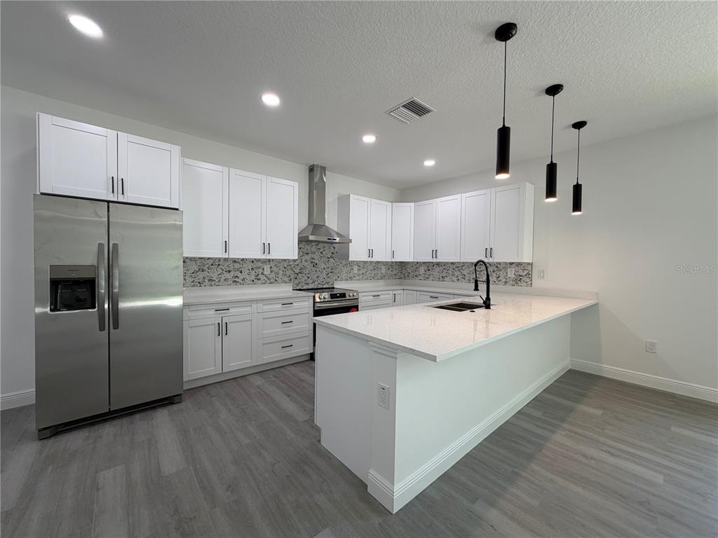 A modern kitchen features white cabinets, stainless steel appliances, a quartz island, and gray flooring — 1611 ILLINOIS STREET, DAYTONA BEACH, FL