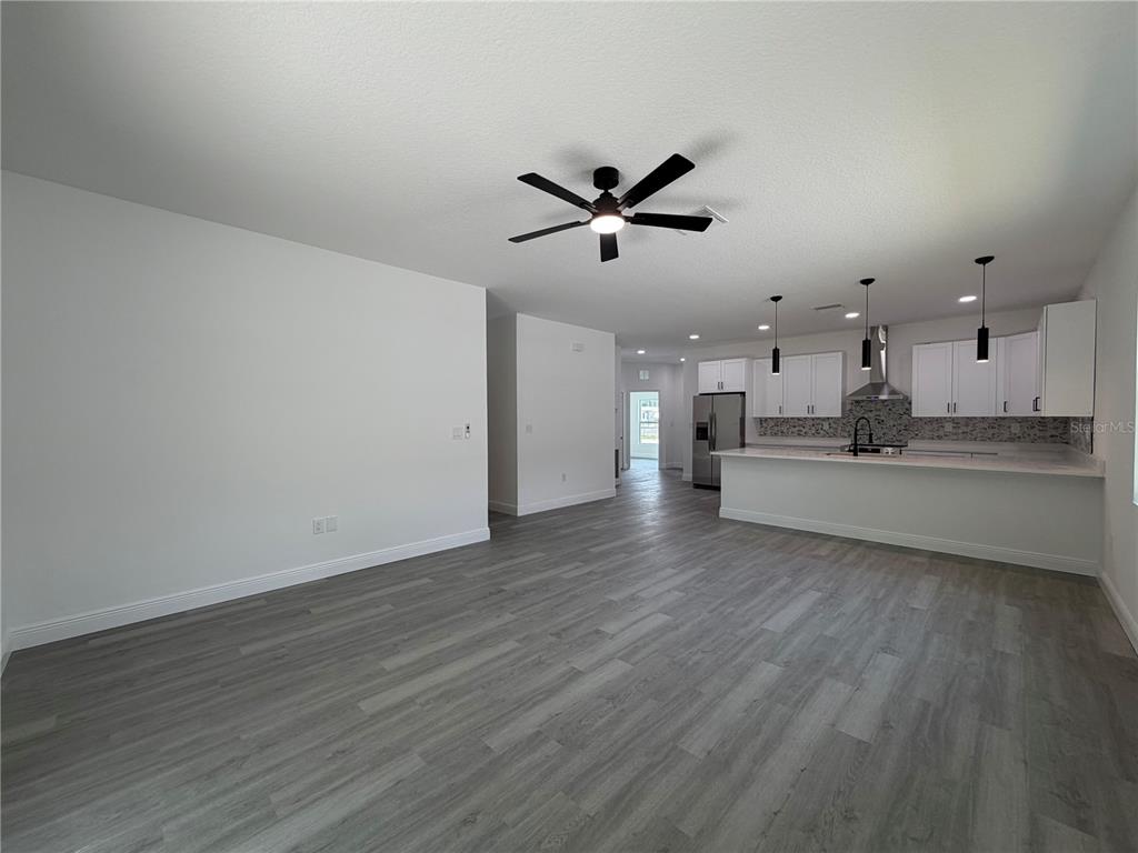 An open-concept living area features gray wood-look flooring, a ceiling fan, and a modern kitchen — 1611 ILLINOIS STREET, DAYTONA BEACH, FL