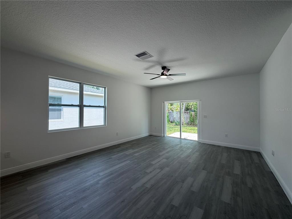 An empty room features gray wood-look flooring, white walls, a ceiling fan, and sliding doors — 1611 ILLINOIS STREET, DAYTONA BEACH, FL