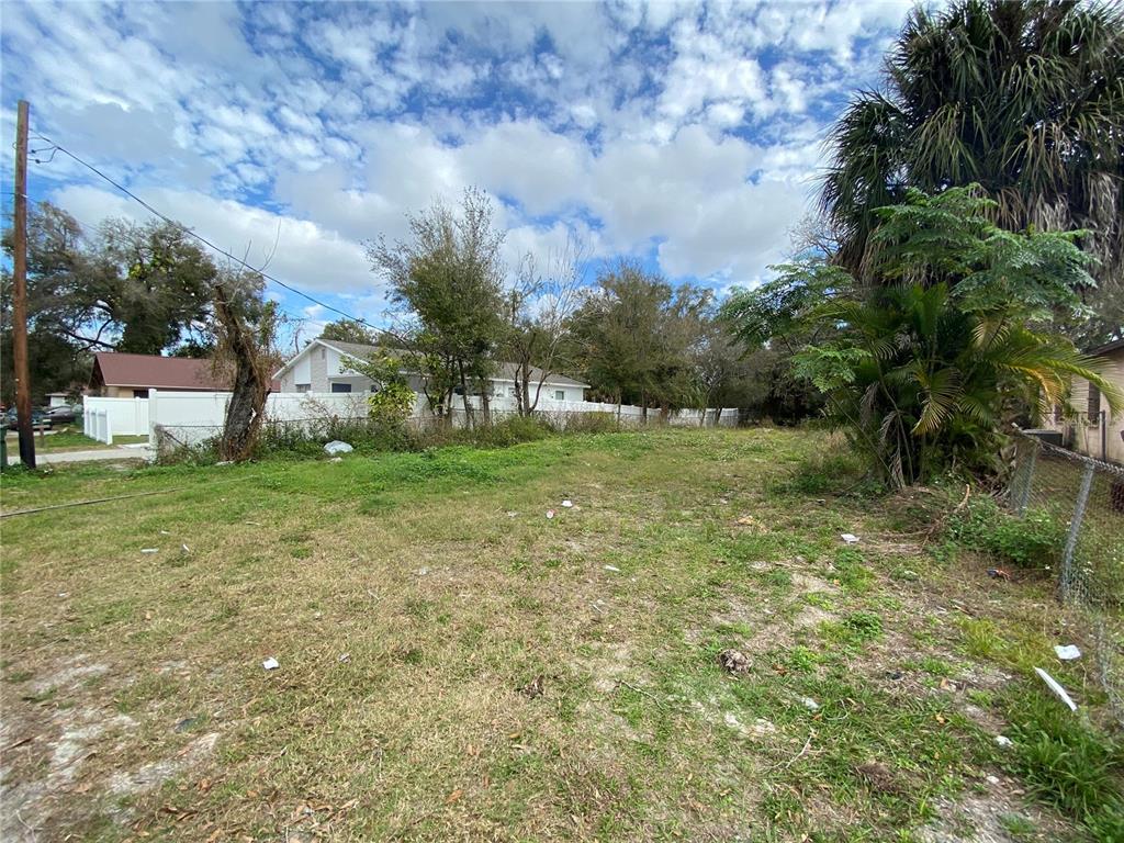 A vacant, grassy residential lot features scattered debris, surrounding trees, and a white fence — 2907 CORD STREET, TAMPA, FL