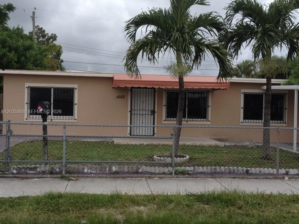 A single-story tan house with a metal awning and a chain-link fence in front — 1550 E 10th Ave, Hialeah FL 33010, HIALEAH, FL