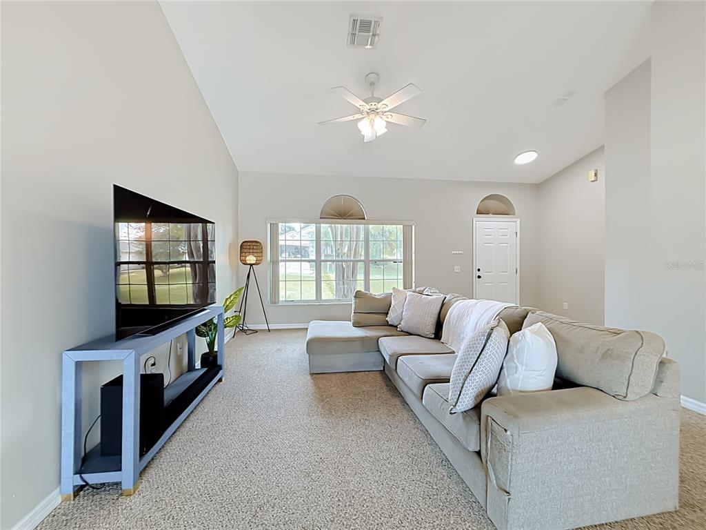 A living room features a sectional sofa, a television on a console, and carpeted flooring — 1364 HILLVIEW DRIVE, CLERMONT, FL