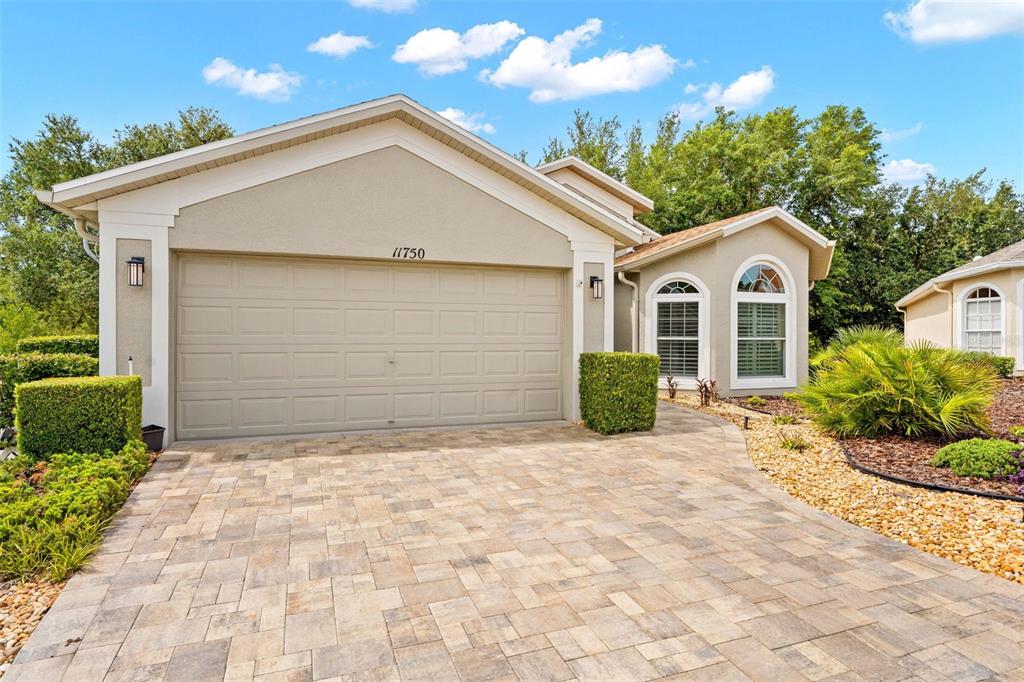 A beige house exterior features a two-car garage, a paver driveway, and arched windows — 11750 TEAPOT COURT, SPRING HILL, FL