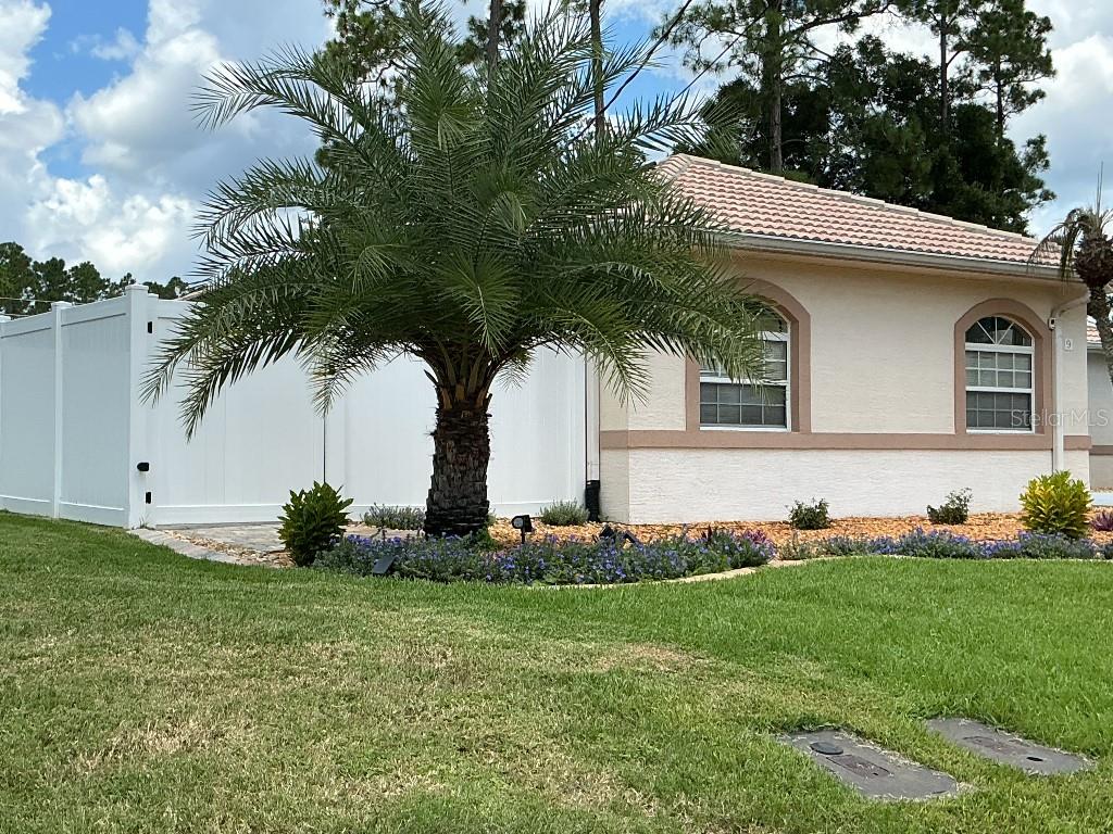 A palm tree stands in front of a tan house with a white vinyl fence — 9 BARKLEY LANE, PALM COAST, FL