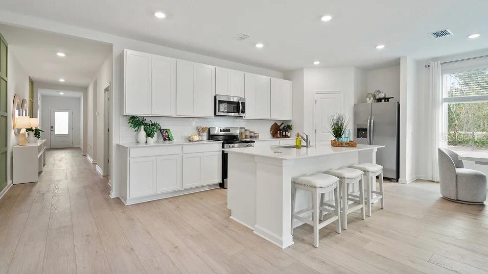 A modern kitchen features white cabinetry, a central island with bar stools, and light wood flooring — 5075 LOGGIA LANE UNIT A, KISSIMMEE, FL