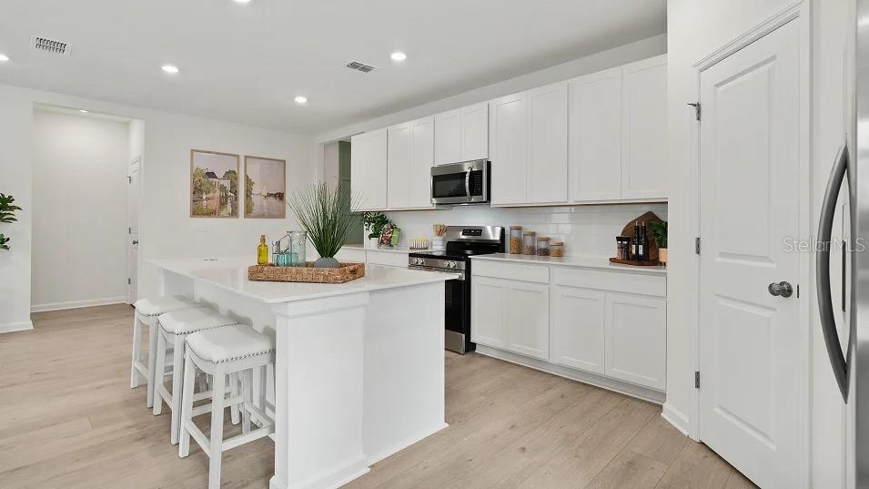 A modern kitchen features white cabinetry, a large island with bar seating, and light flooring — 5075 LOGGIA LANE UNIT A, KISSIMMEE, FL