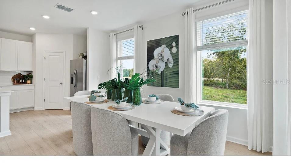 A bright dining area features a white table, upholstered chairs, and large windows with views — 5075 LOGGIA LANE UNIT A, KISSIMMEE, FL
