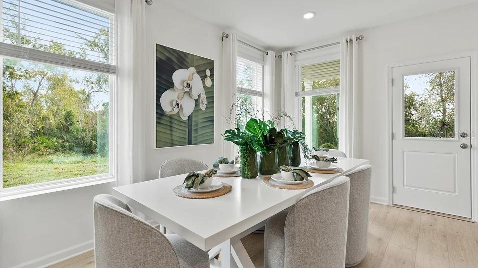 A bright dining room features a white table, upholstered chairs, and large windows with greenery — 5075 LOGGIA LANE UNIT A, KISSIMMEE, FL