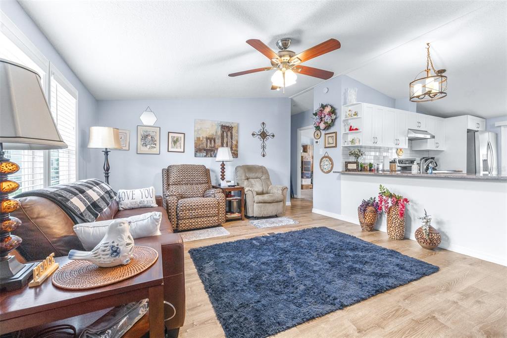 A living room with light blue walls, wood-look flooring, a dark blue rug, and an open kitchen — 3041 SHORT LEAF STREET, WESLEY CHAPEL, FL