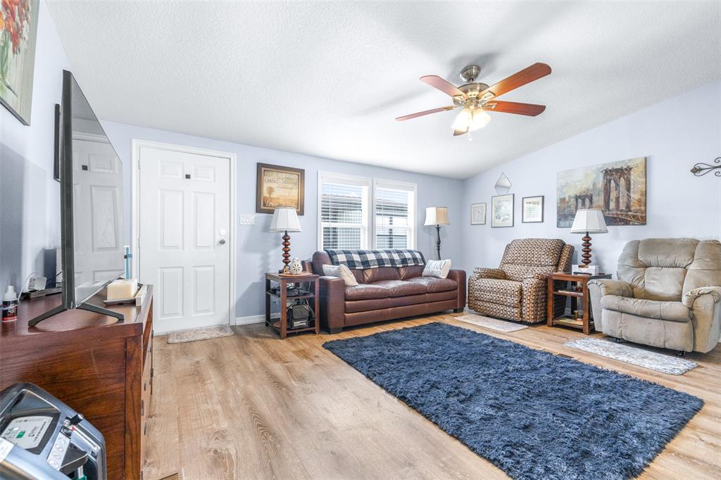 A living room features a brown leather sofa, two recliners, a blue rug, and wood-look flooring — 3041 SHORT LEAF STREET, WESLEY CHAPEL, FL