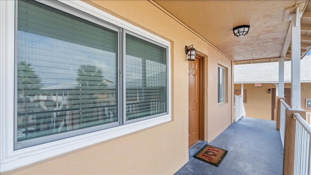 An exterior walkway leads to a brown door with a "JOY" mat outside unit 304 — 411 N HALIFAX AVENUE UNIT 304, DAYTONA BEACH, FL