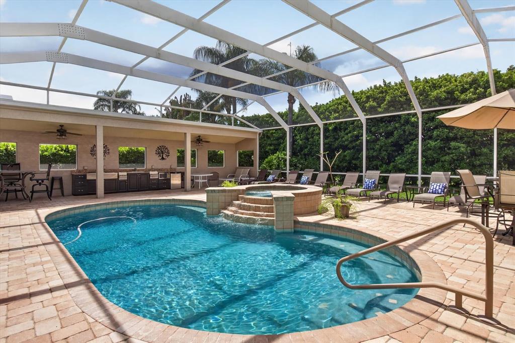 A screened-in patio features a swimming pool with an integrated hot tub and outdoor kitchen — 4052 CAPITOL DRIVE, PALM HARBOR, FL