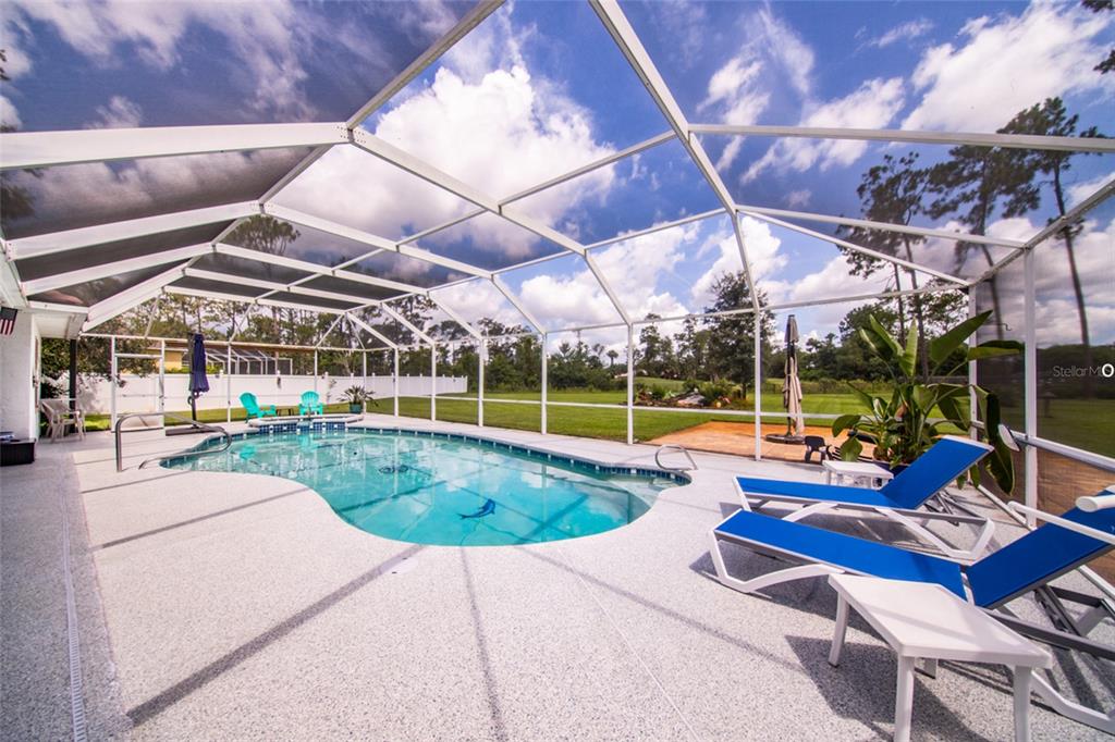 A screened-in swimming pool area features lounge chairs on a speckled concrete patio — 87 EASTWOOD DRIVE, PALM COAST, FL