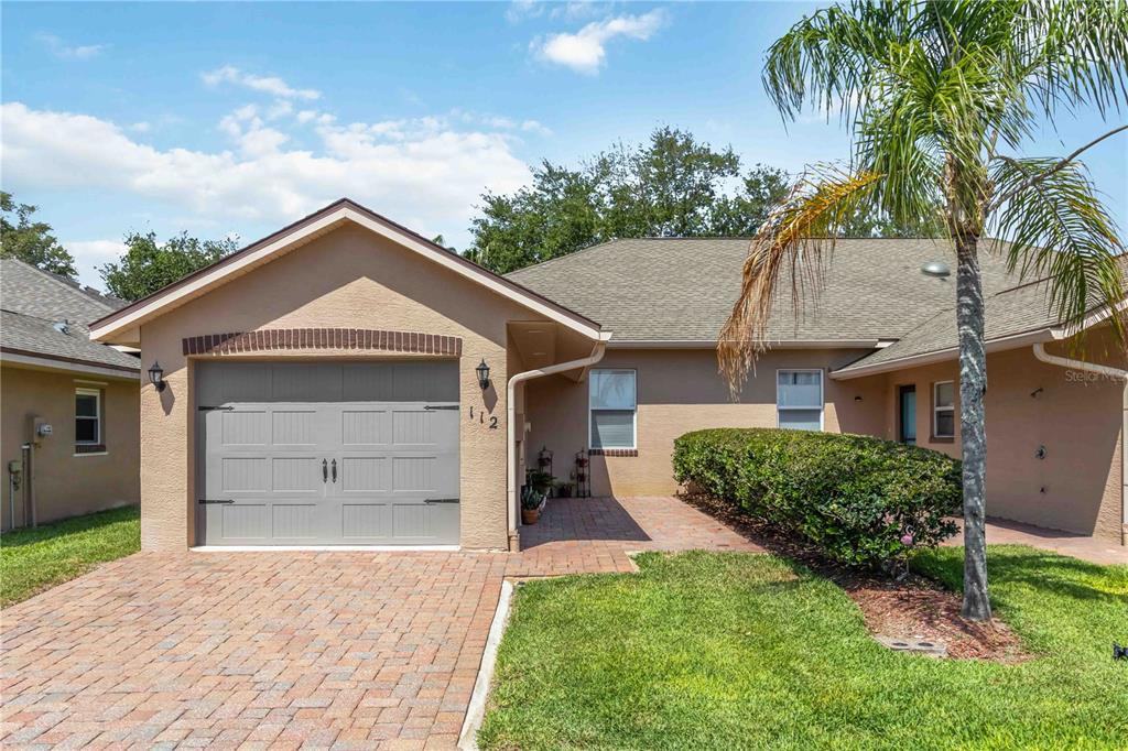 A single-story house with a tan stucco exterior, a gray garage door, and a palm tree — 112 TUSCANY VILLAS DRIVE UNIT 112, EDGEWATER, FL