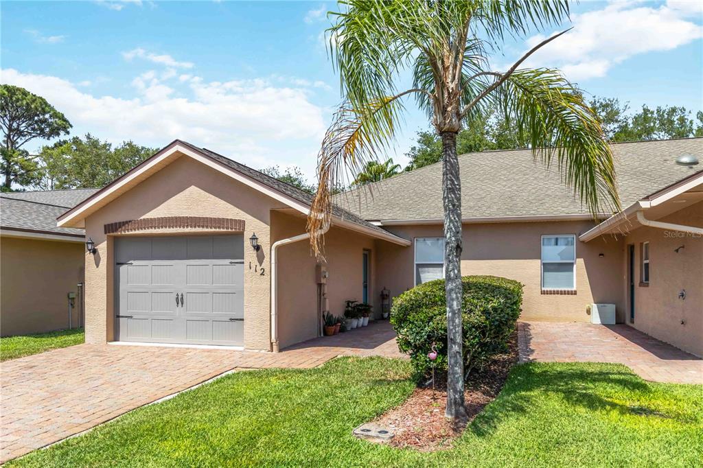 A single-story house exterior features a tan stucco facade, a gray garage, and a palm tree — 112 TUSCANY VILLAS DRIVE UNIT 112, EDGEWATER, FL