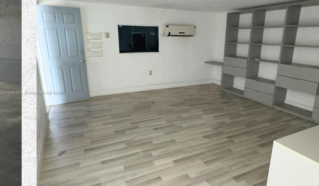 A room with light wood-look flooring, a blue door, a wall-mounted air conditioner, and shelving — 4201 NW 37th Ct # B, Hialeah FL 33142, HIALEAH, FL