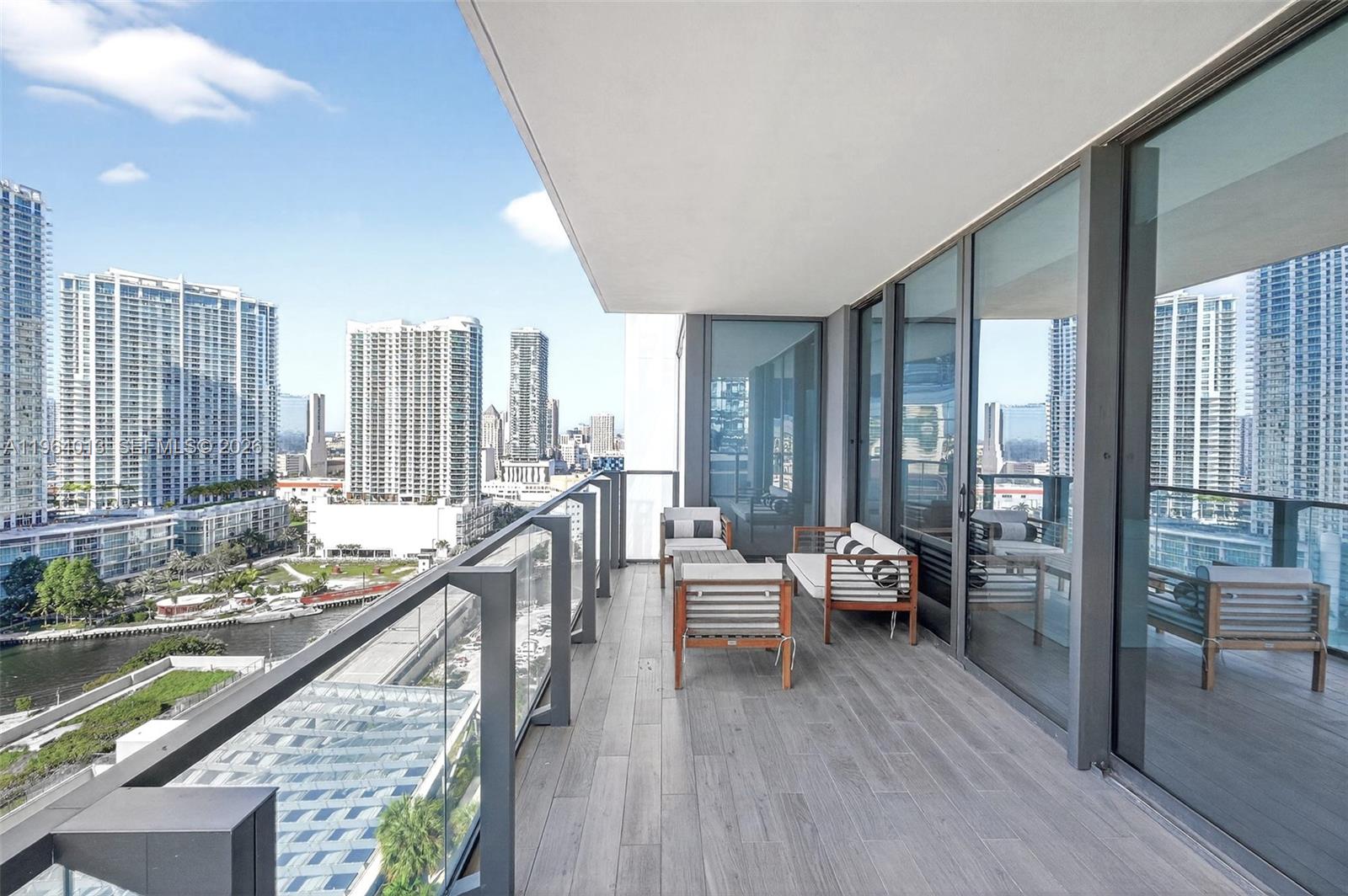 A modern balcony with wood-look tile flooring overlooks a city skyline and a river — 68 SE 6th St # 1702, Miami FL 33131, MIAMI, FL
