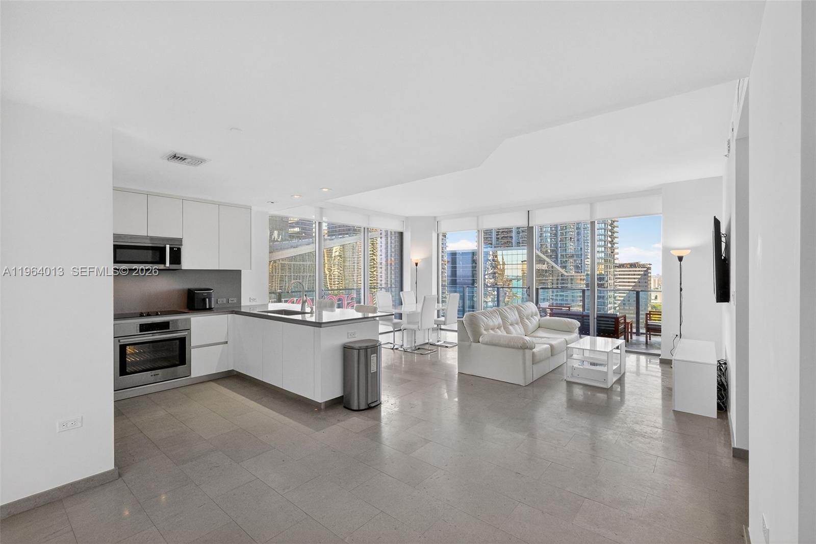 A modern open-concept kitchen and living area with white cabinetry, tile floors, and balcony views — 68 SE 6th St # 1702, Miami FL 33131, MIAMI, FL