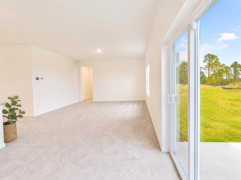 An empty room with beige carpet, white walls, and a sliding glass door to a yard — 2150 GOLD DUST DRIVE, CLERMONT, FL